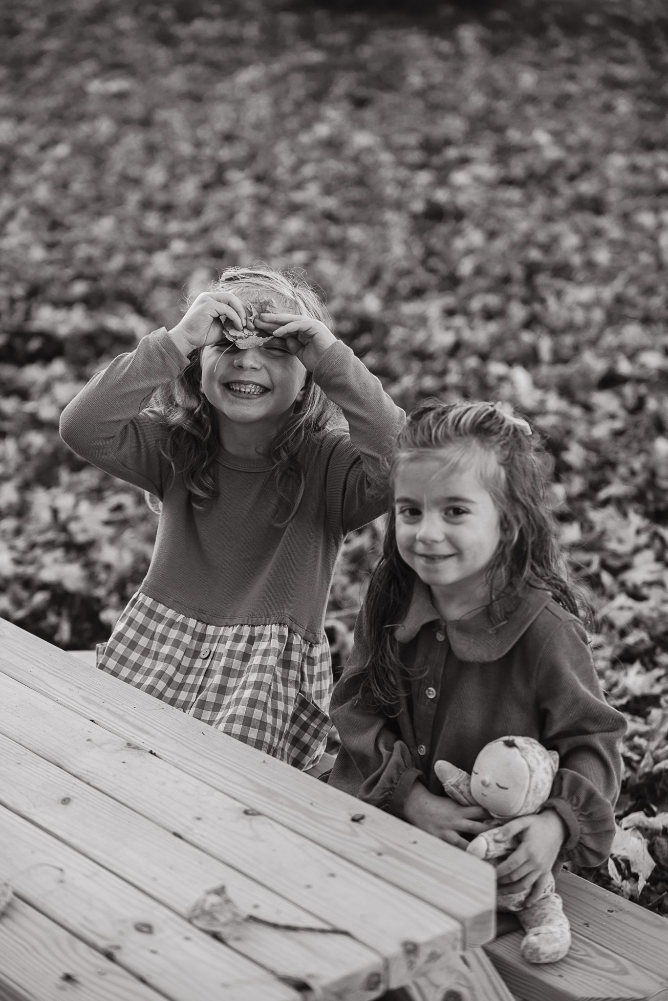 Black and white photo of two children playing and laughing together on a wooden deck surrounded by fallen leaves.