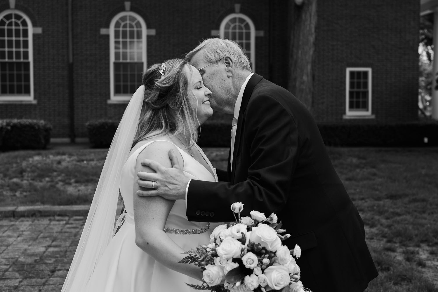 Bride and groom share a romantic moment outside a brick church building.