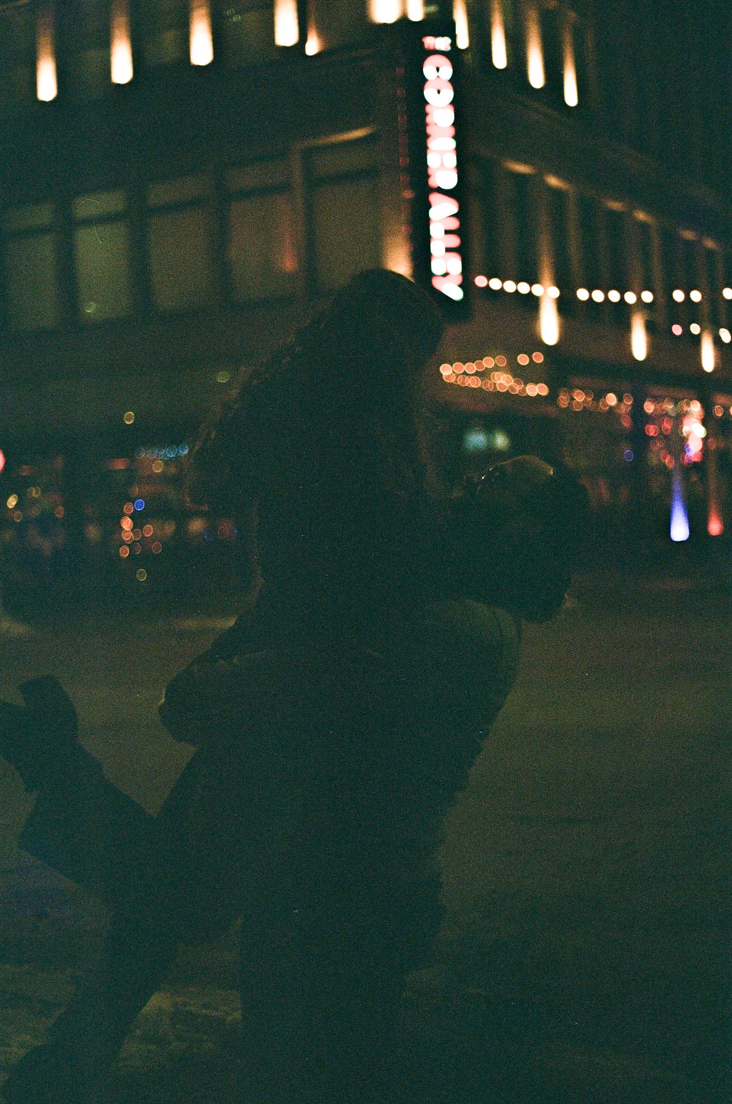 Dark silhouettes of people against a nighttime cityscape with glowing lights and string lights in the background.