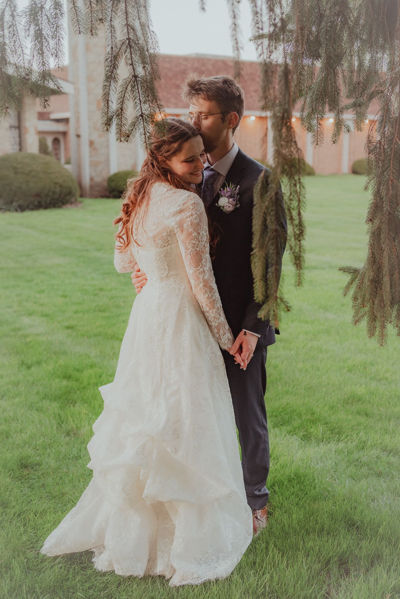 Romantic wedding couple poses under weeping willow tree in garden setting.