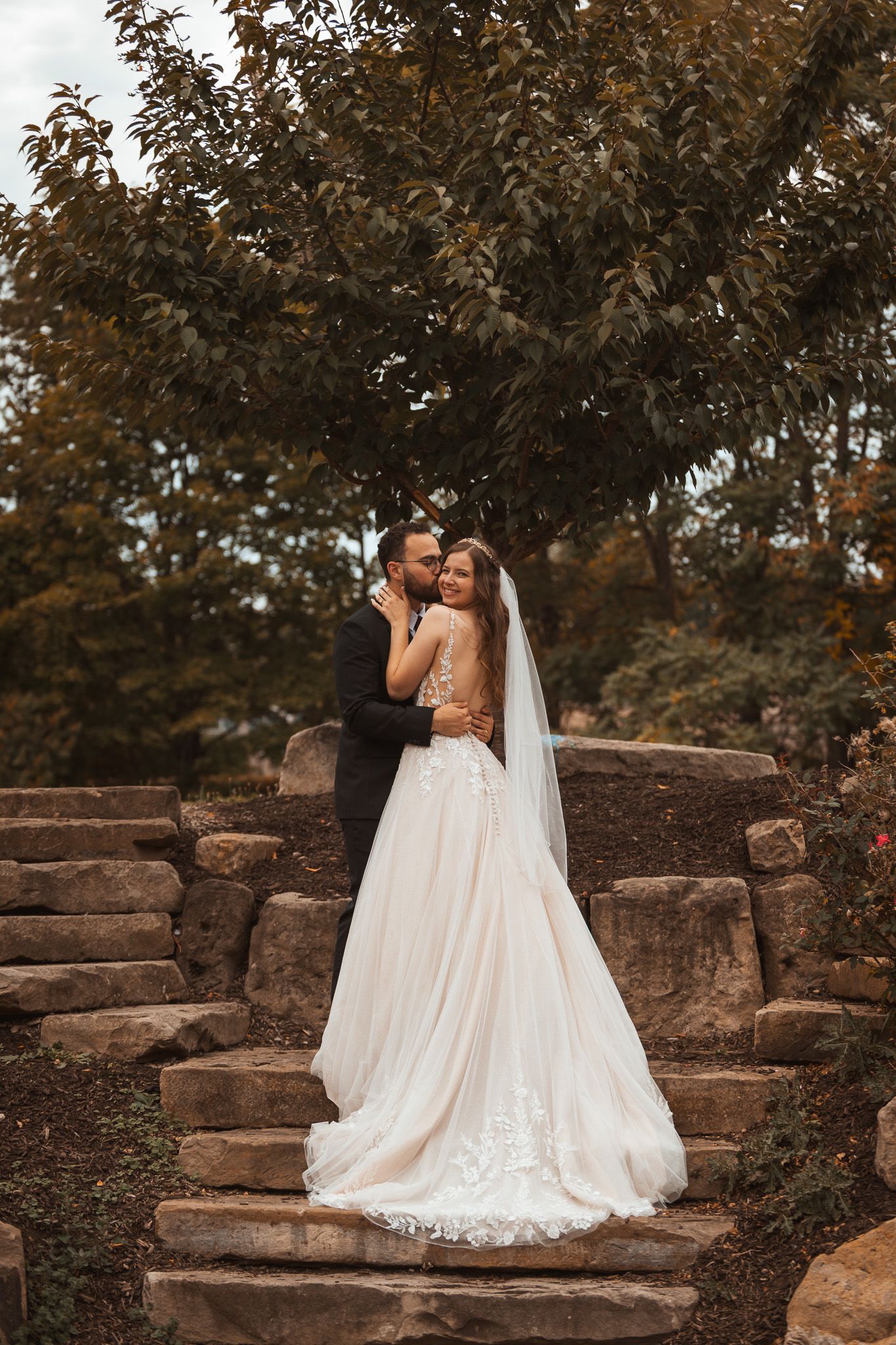 Wedding couple poses on rustic stone steps surrounded by autumn foliage.