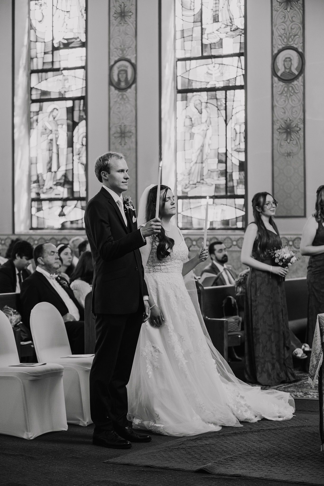 Wedding ceremony in progress inside church with beautiful stained glass windows.