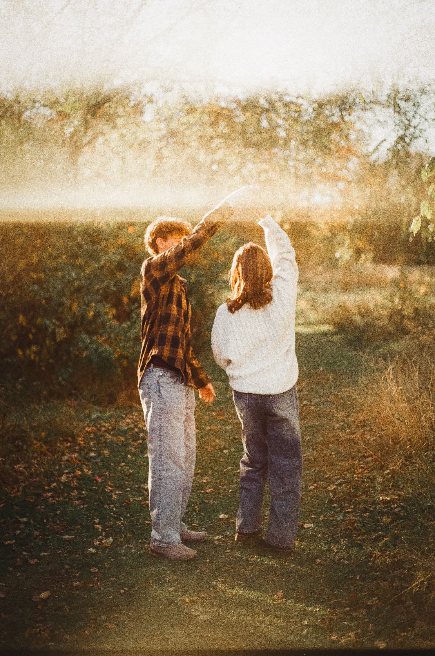 Two children explore a misty autumn field together during golden hour as sunlight filters through the trees.