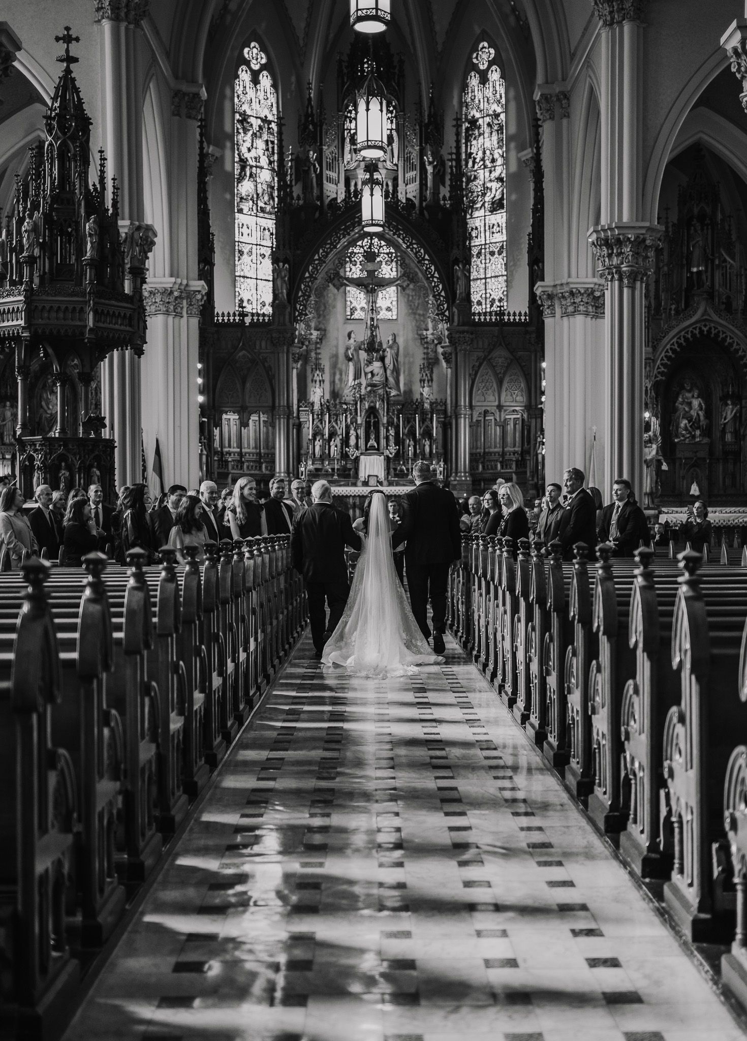 Black and white photo of a church aisle during a wedding ceremony with Gothic architecture.