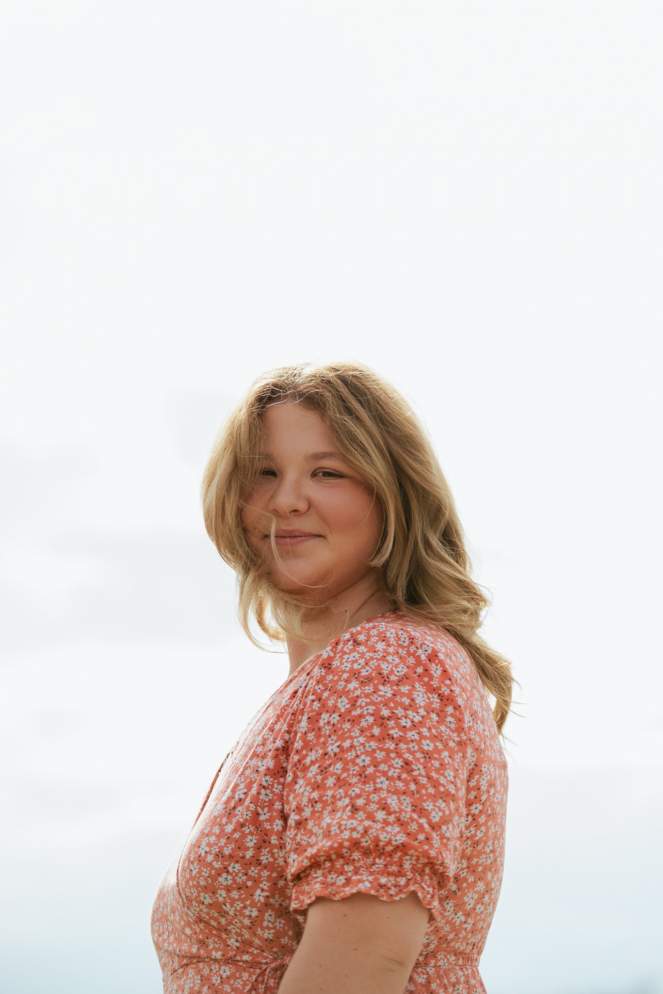 Portrait of someone wearing a coral floral dress against a bright sky background.