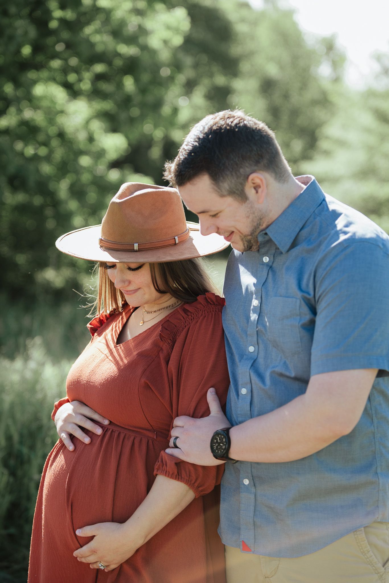 A couple in casual attire shares an intimate moment outdoors during a maternity photoshoot.