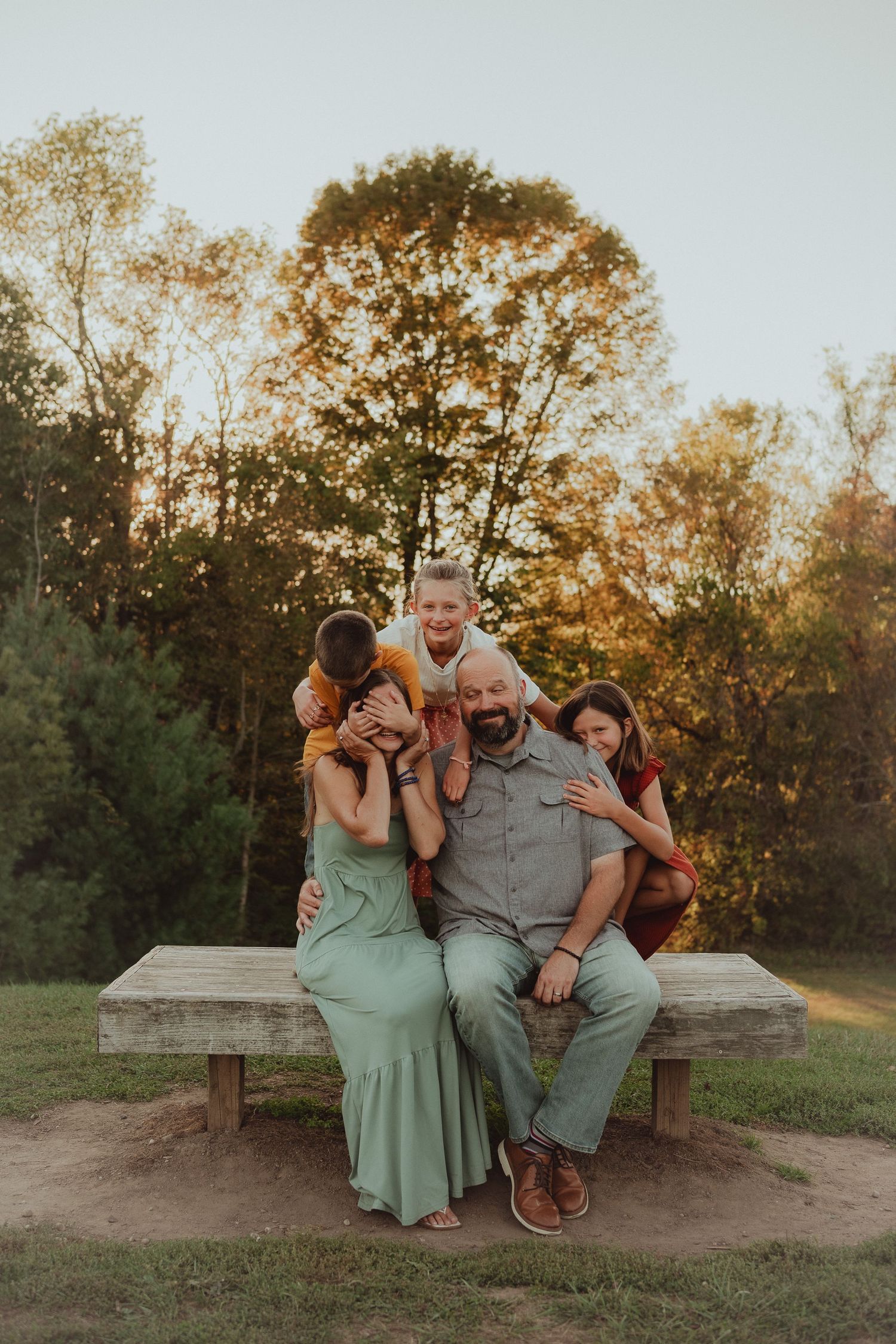 A family sits together on a stone wall during a golden sunset photo session in casual outdoor attire.