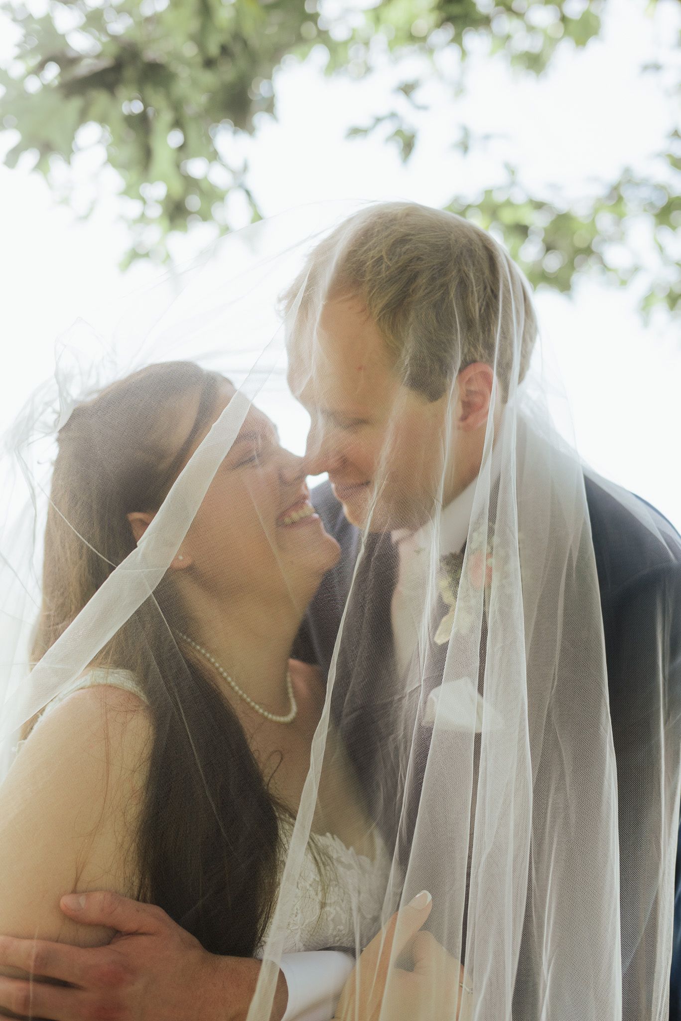 Romantic moment under a flowing white veil with soft natural lighting.