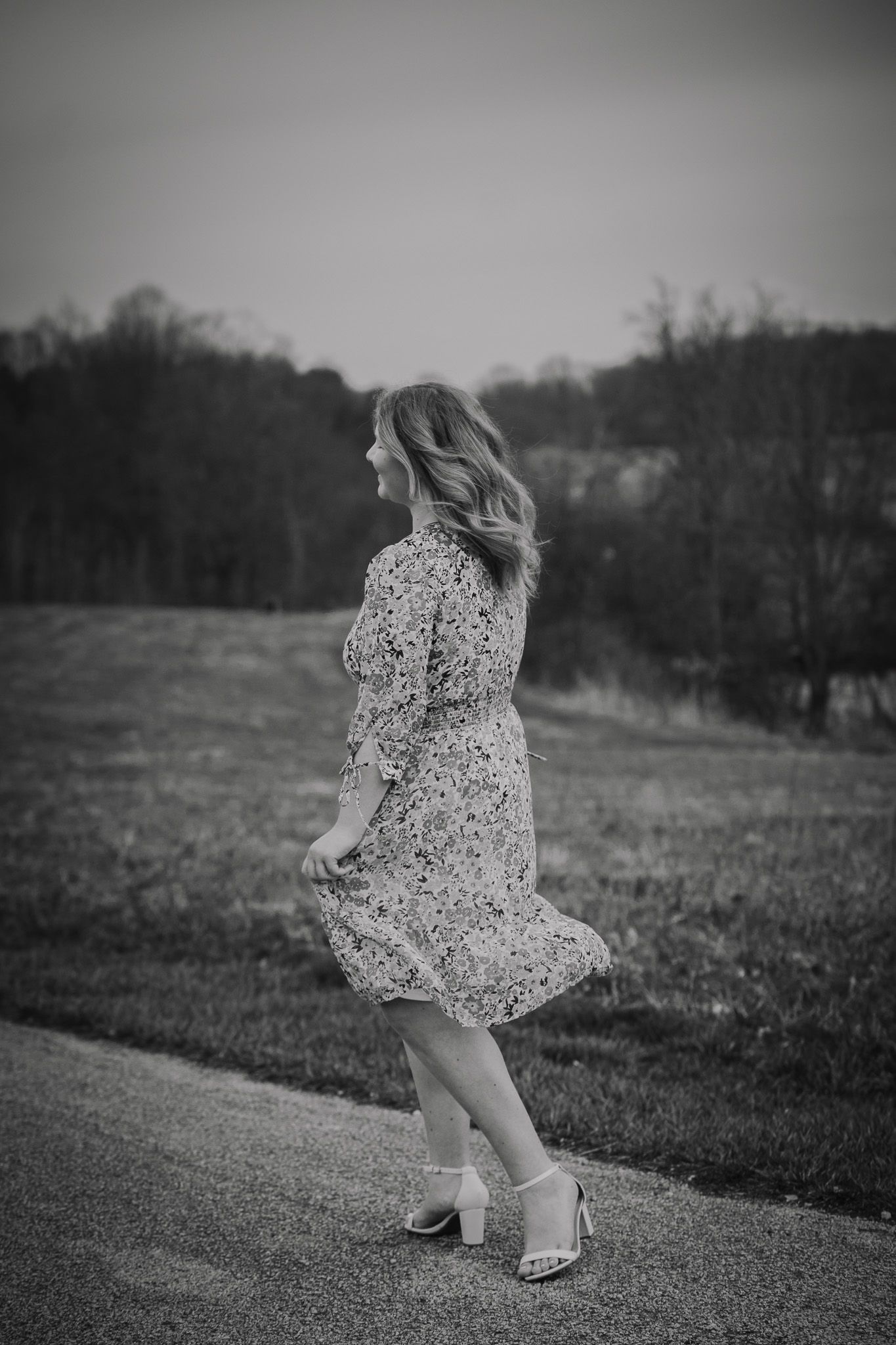 Person in floral dress twirling on a country path in black and white photography.