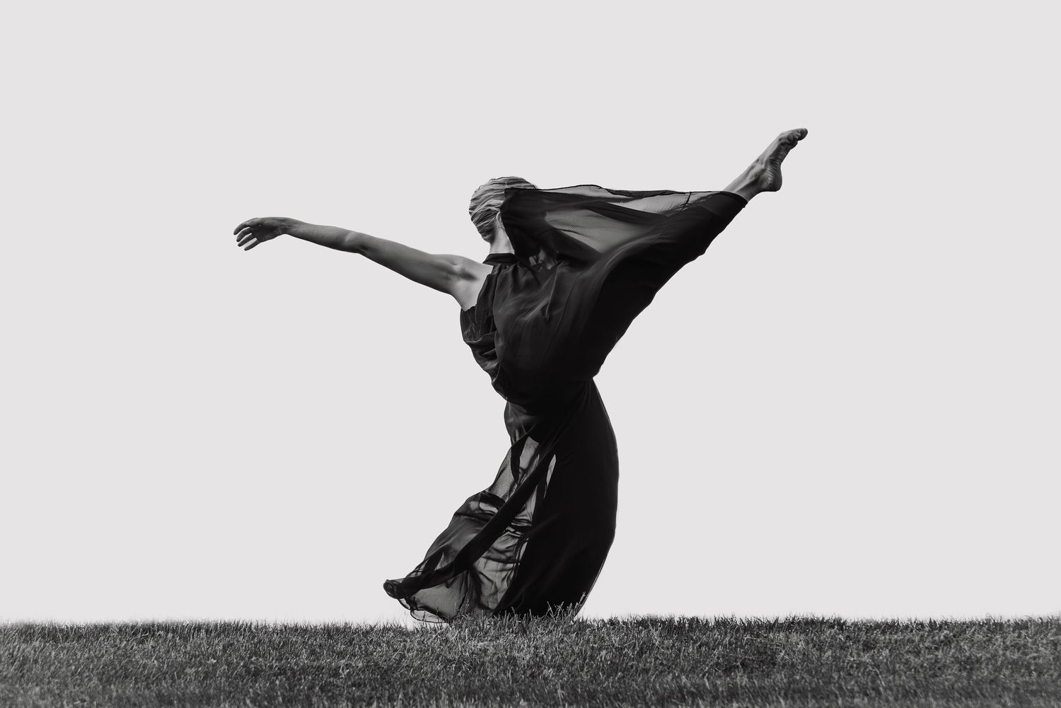 Black and white silhouette of a bride's veil flowing dramatically in the wind against a cloudy sky.