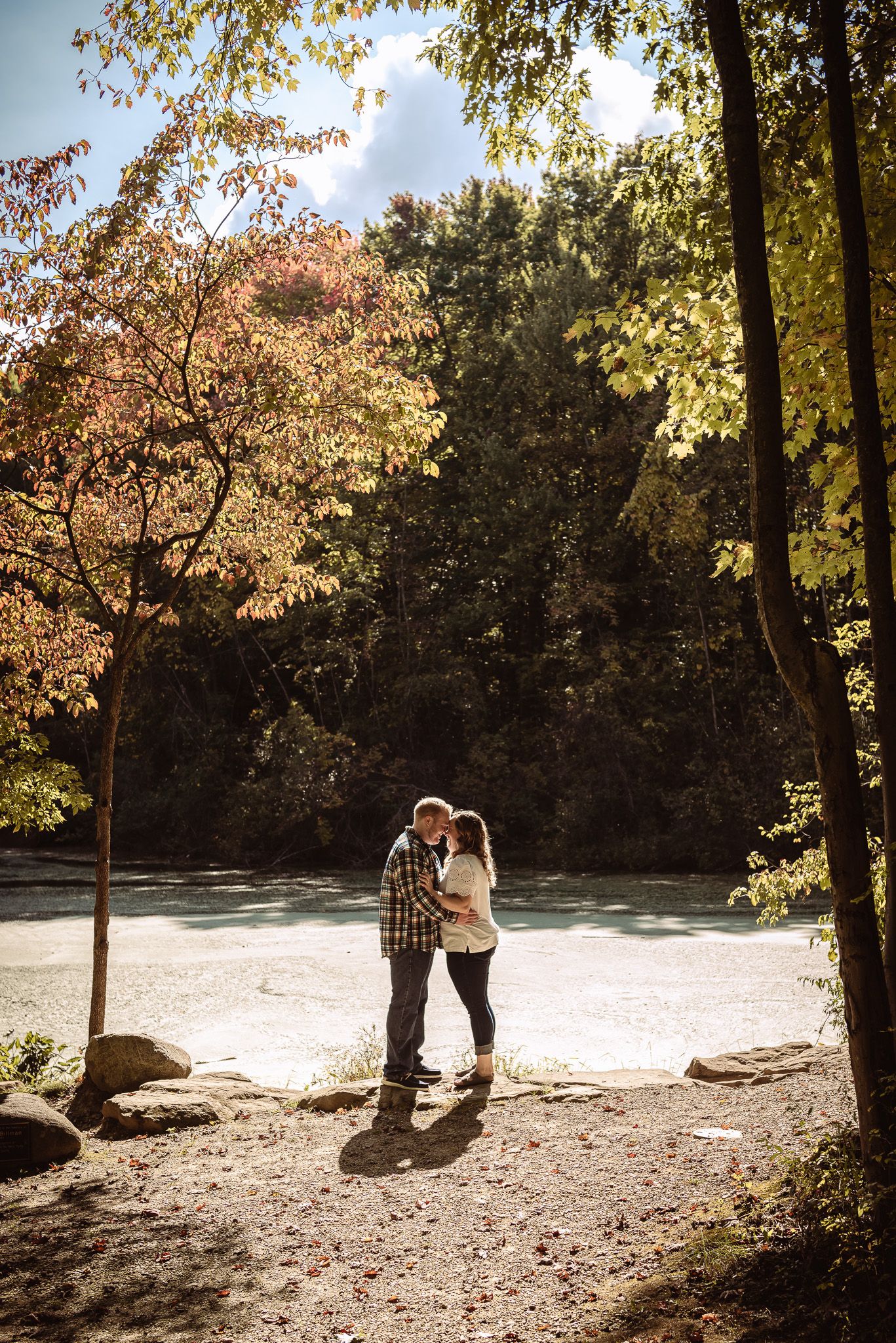Couple embracing on forest path with sunlight streaming through autumn trees.