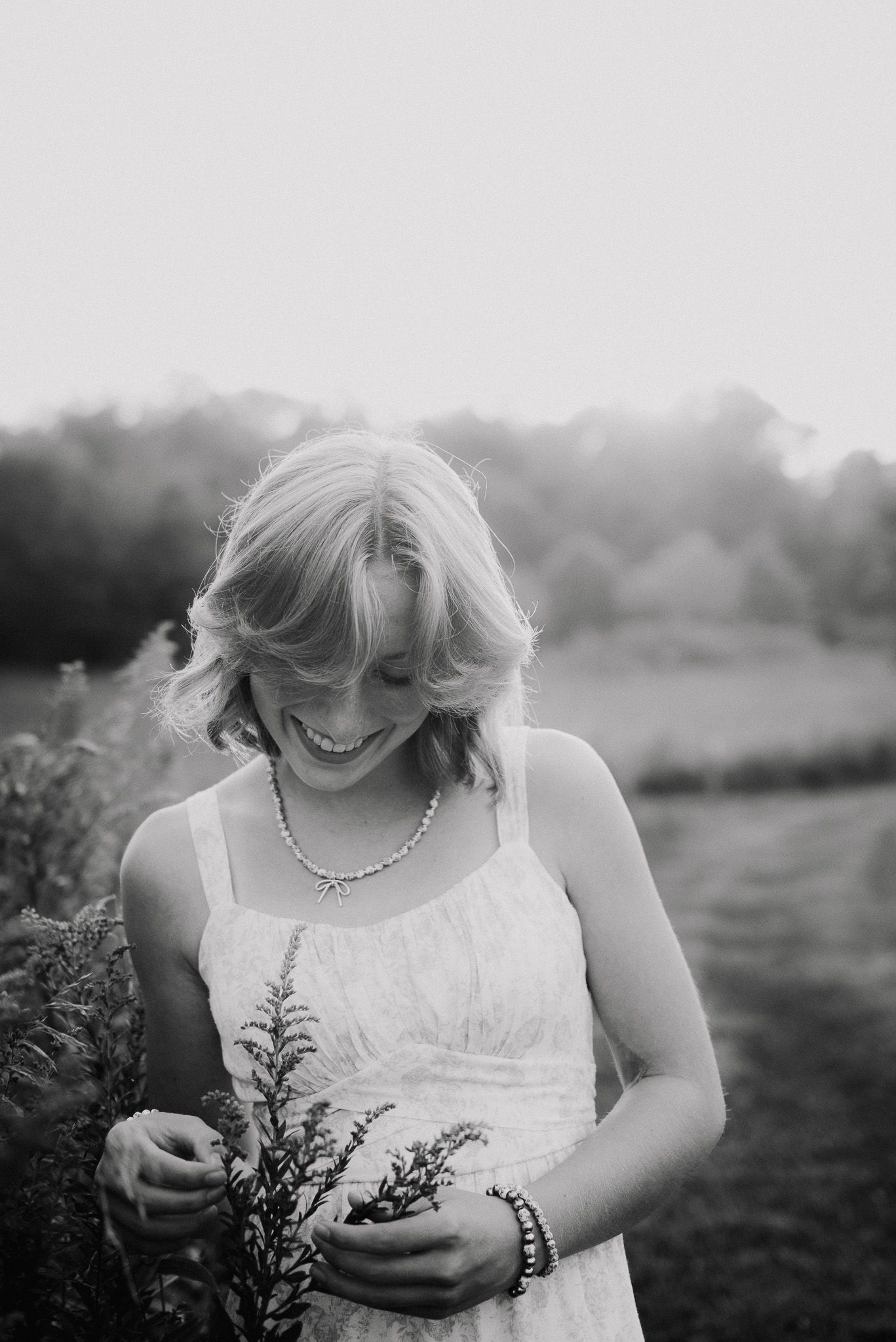 Black and white photo of someone in white dress holding wildflowers and laughing.