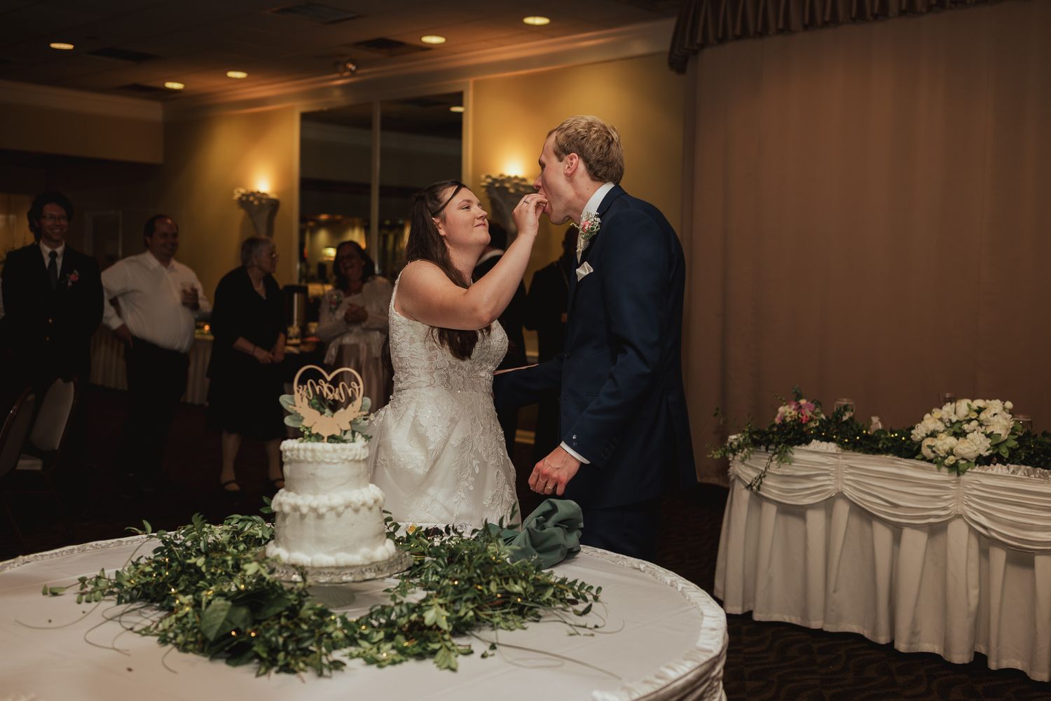 Wedding reception setup with elegant table settings and a traditional white tiered cake.