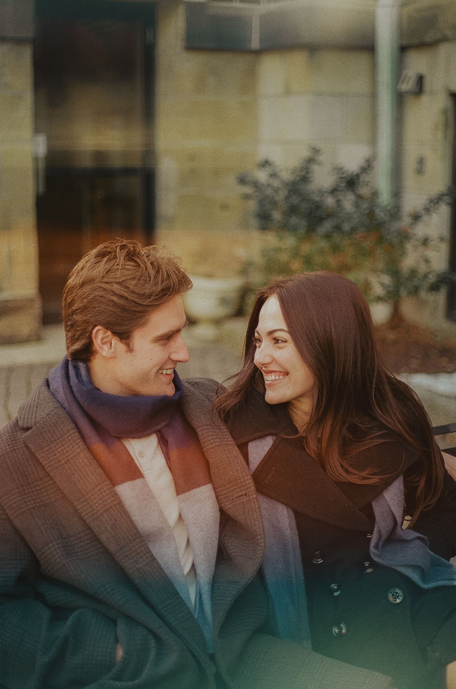 A romantic couple shares intimate moments while sitting together outdoors in autumn clothing.