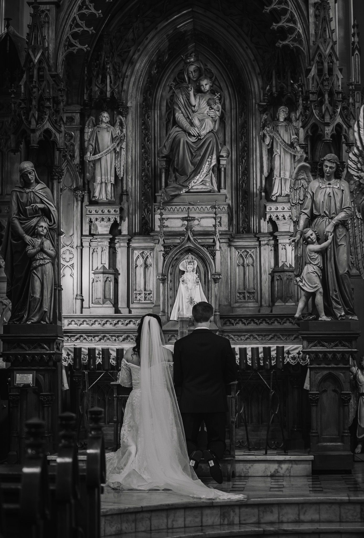 Black and white photo of a couple standing before an ornate church altar during their wedding.