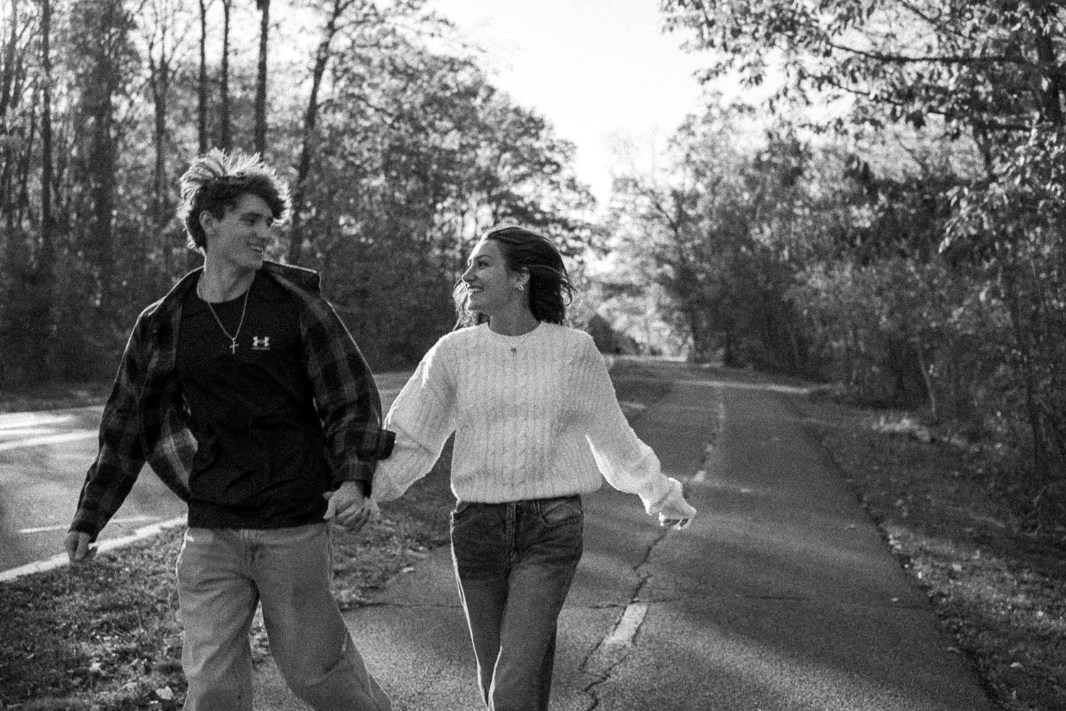 A couple walking together and holding hands on a tree-lined path in black and white photography.