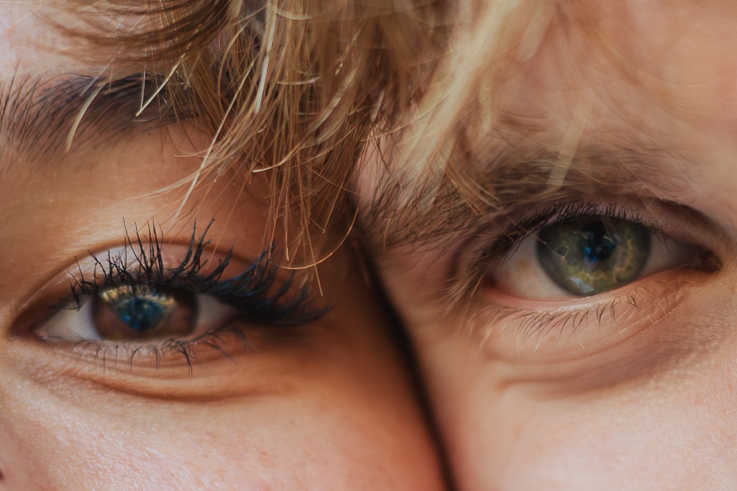 Close-up of two people's eyes side by side, showcasing green and blue eyes with natural light.