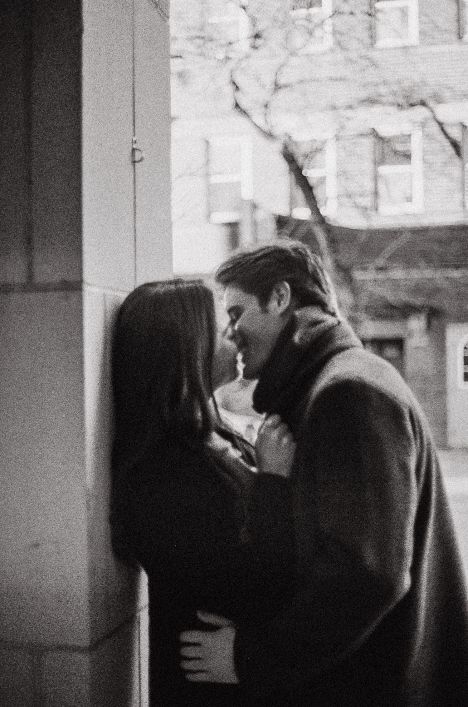A romantic black and white photograph of a couple sharing an intimate moment near a doorway.