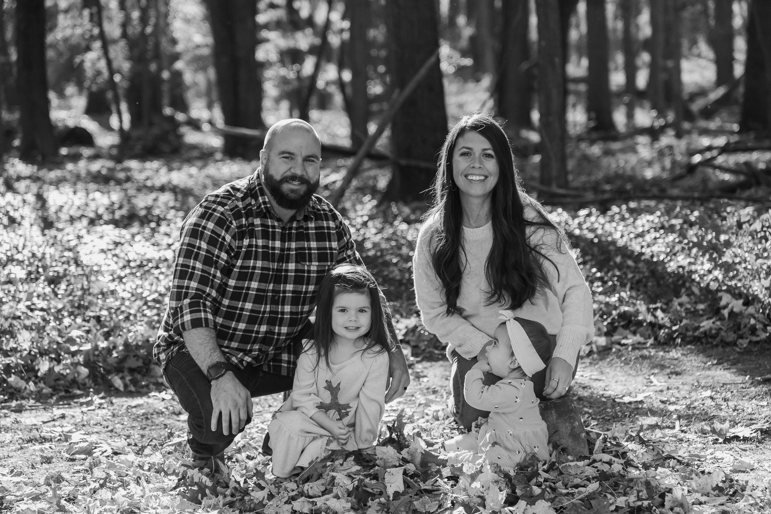 Black and white portrait of family sitting together in forest setting.