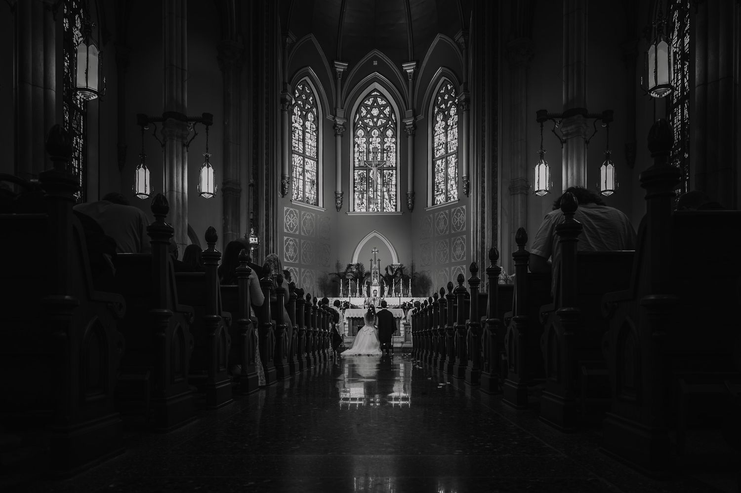 Black and white wedding ceremony photo inside a grand cathedral with stained glass windows and guests seated in pews.