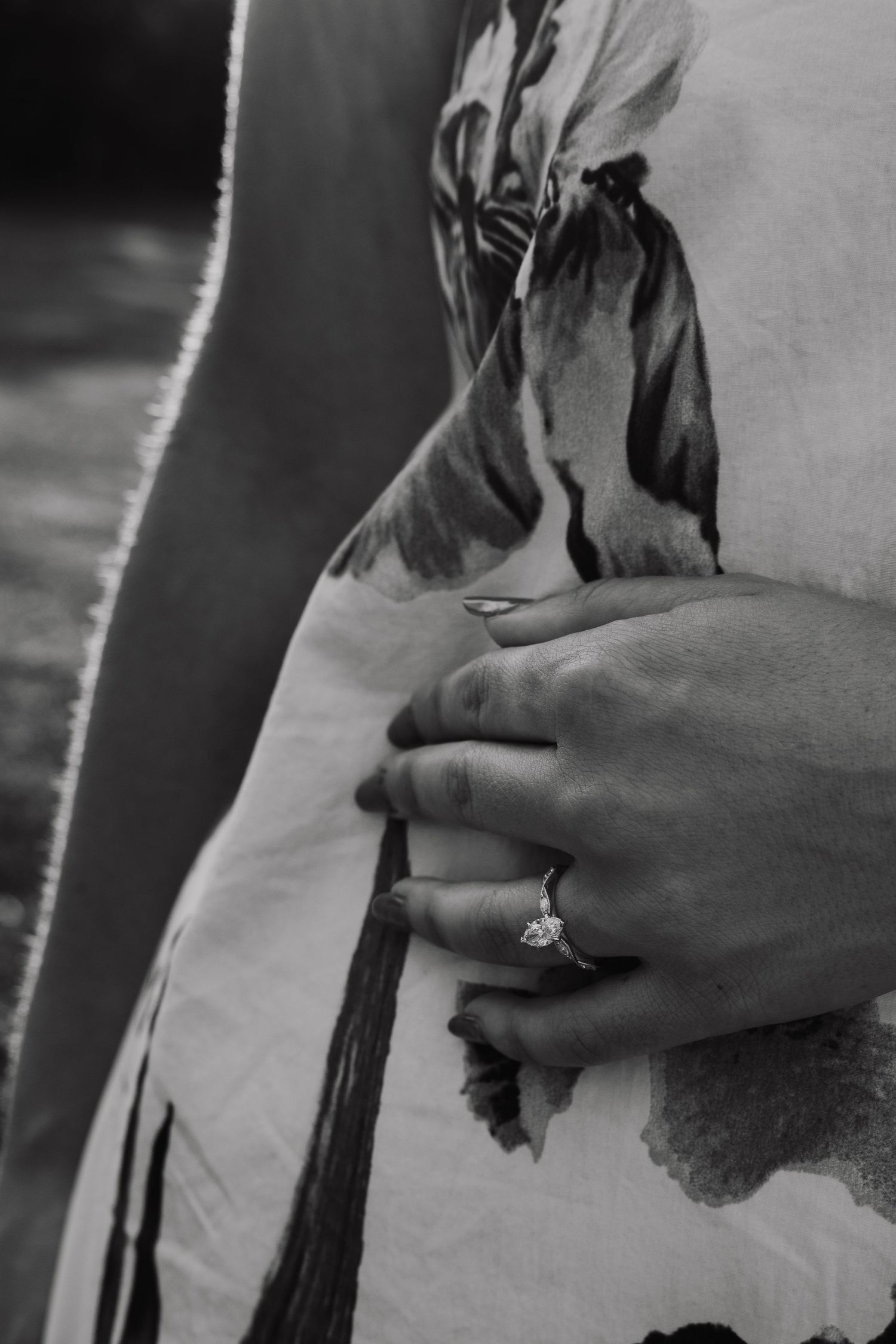 Black and white close-up of a hand with an engagement ring resting on a floral dress.