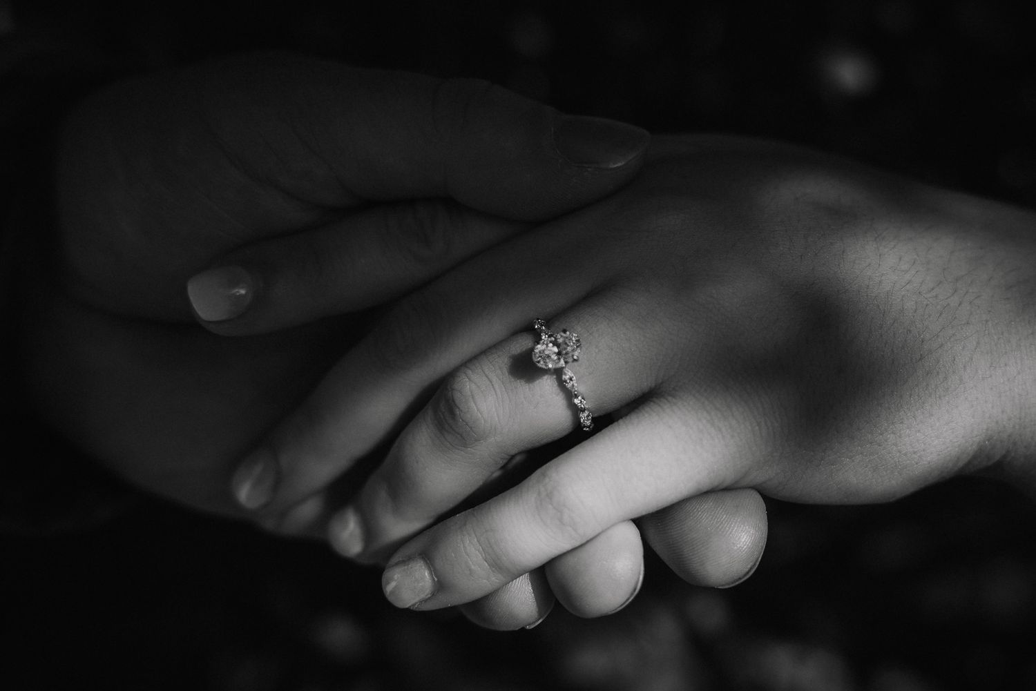 Close-up black and white photo of hands with engagement ring.