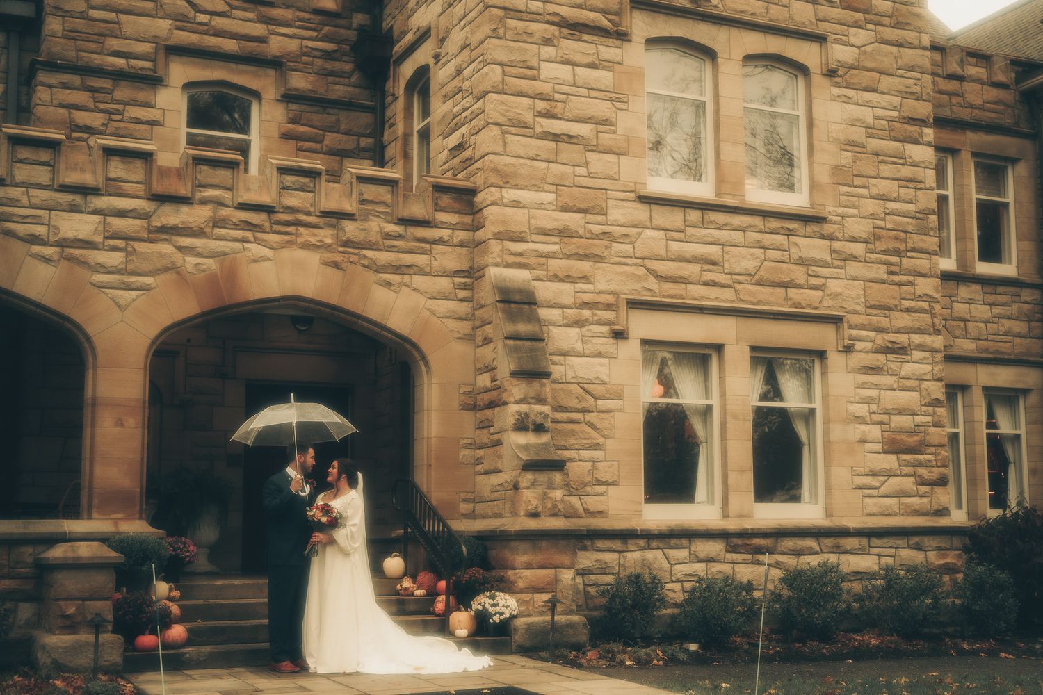 A couple shares an intimate moment under an umbrella at the entrance of a grand stone building.