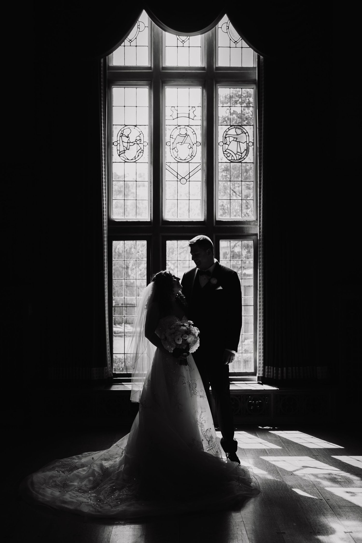 Silhouette of bride and groom embracing before a stunning stained glass window in black and white wedding portrait.