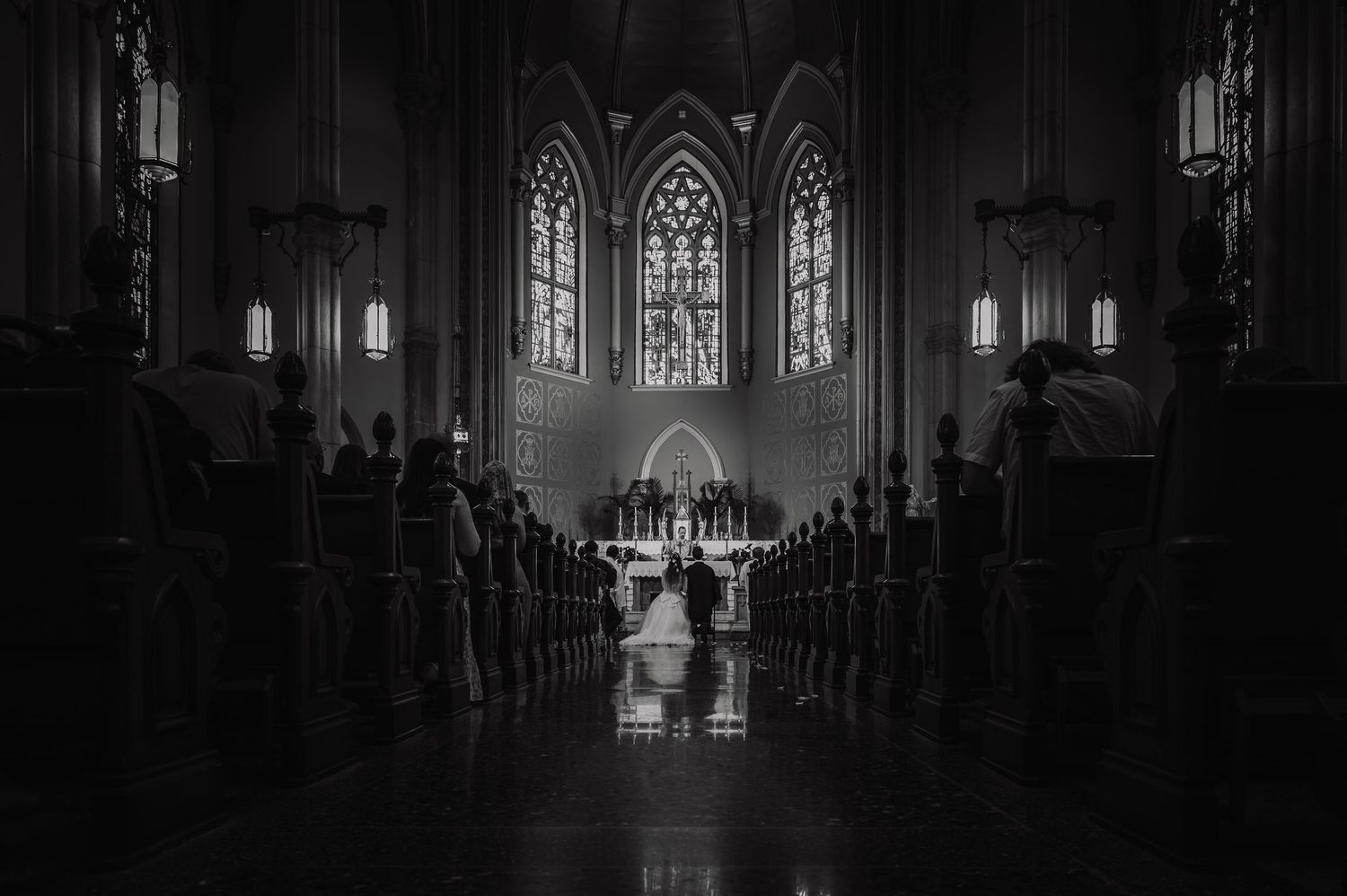 Black and white photo of a wedding ceremony inside a grand cathedral with Gothic stained glass windows.