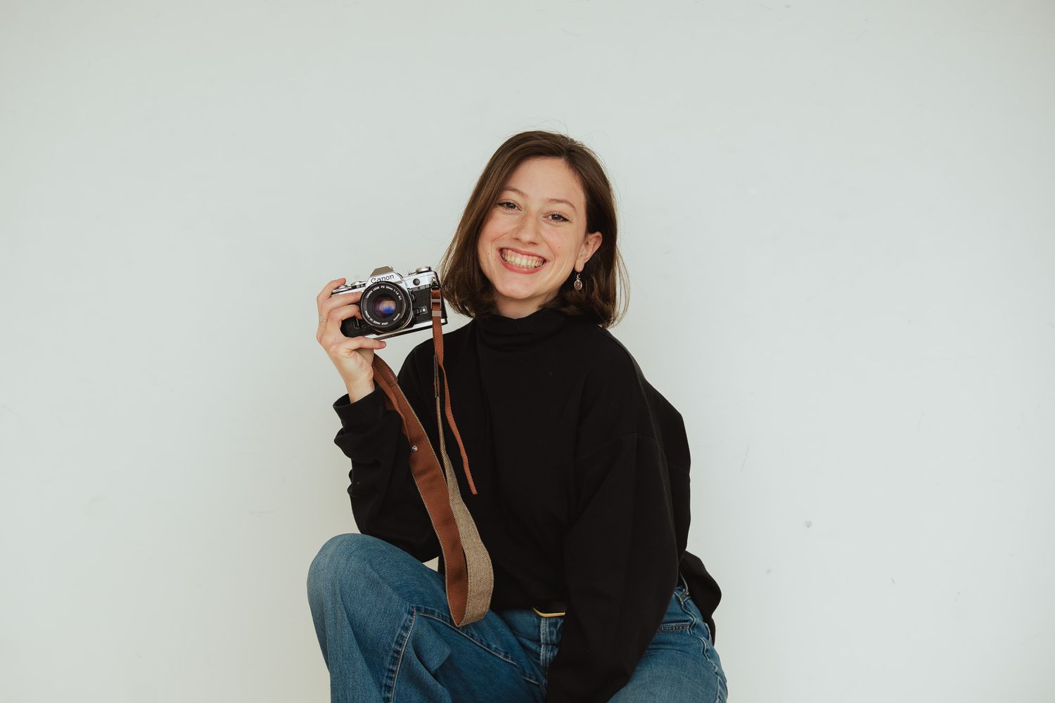 Person in black turtleneck sweater poses with vintage camera against white background.