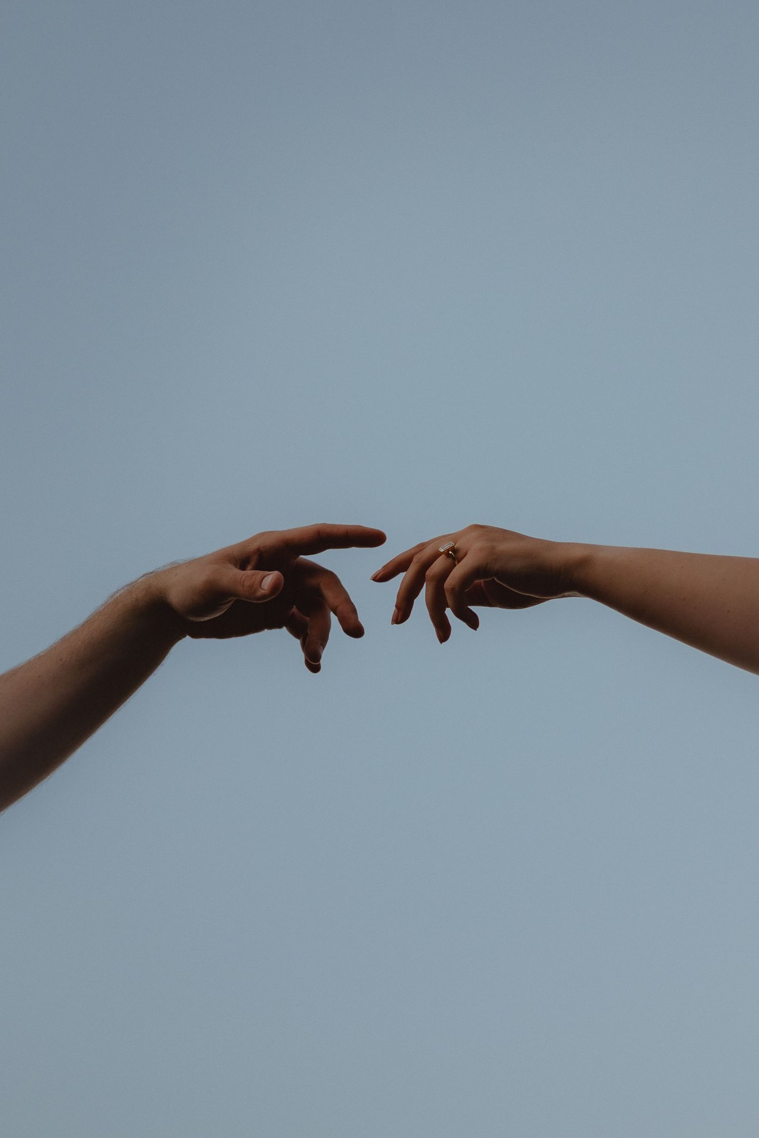 Two hands reaching toward each other against a clear blue sky, reminiscent of Michelangelo's Creation of Adam.