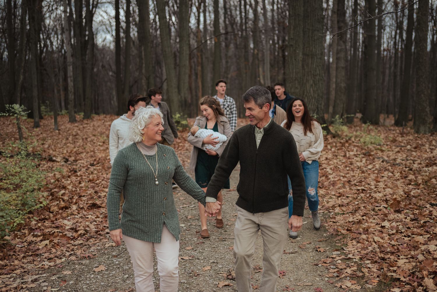 A casual group walking and laughing together on a leaf-covered forest path.