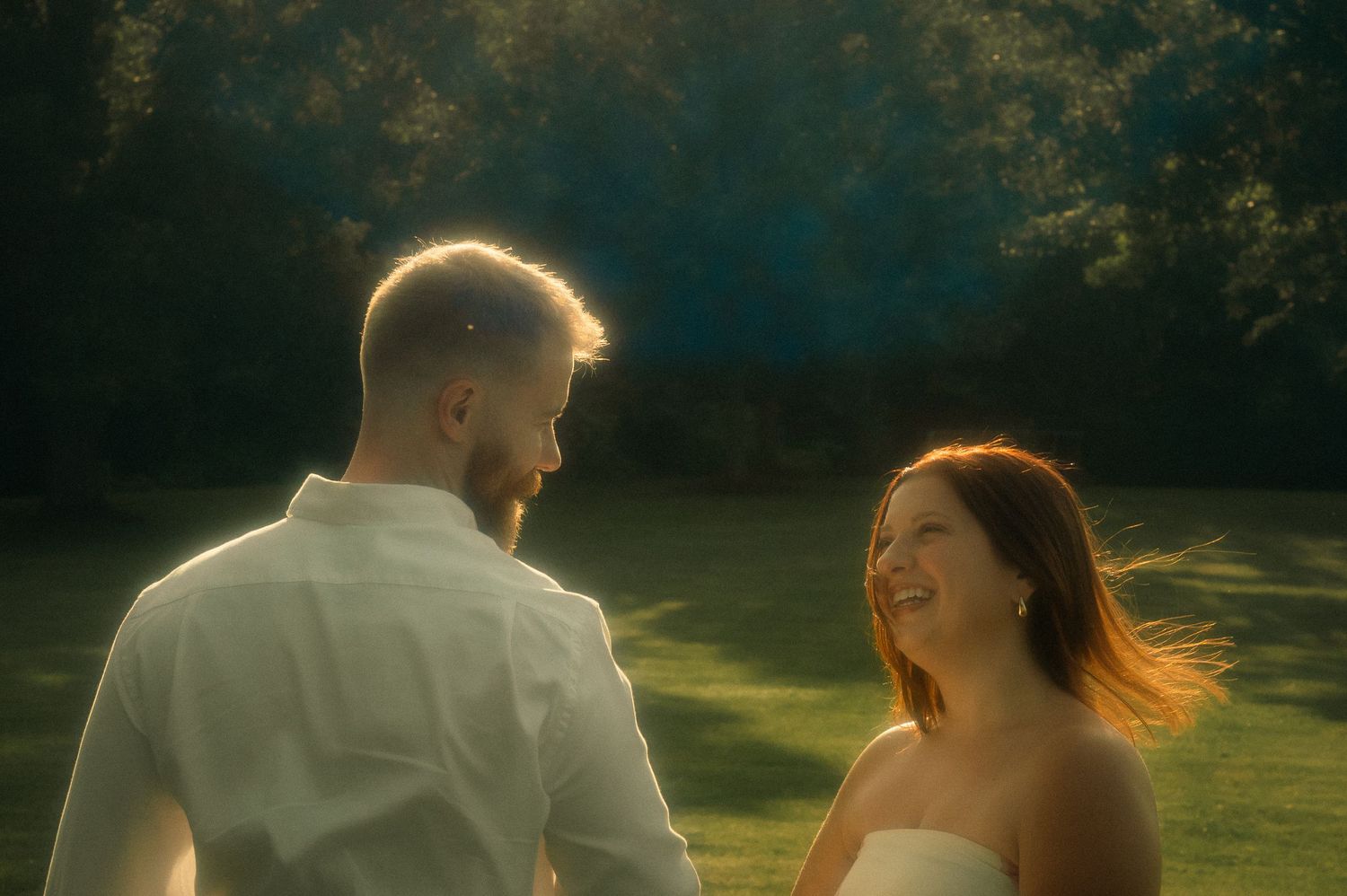 Couple sharing a romantic moment outdoors in golden sunlight with lush green trees in the background.