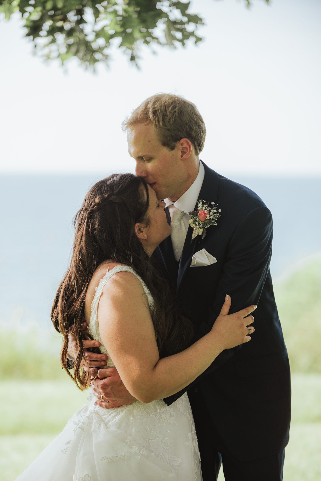 A romantic wedding couple shares intimate kisses in a series of outdoor portraits by the water.