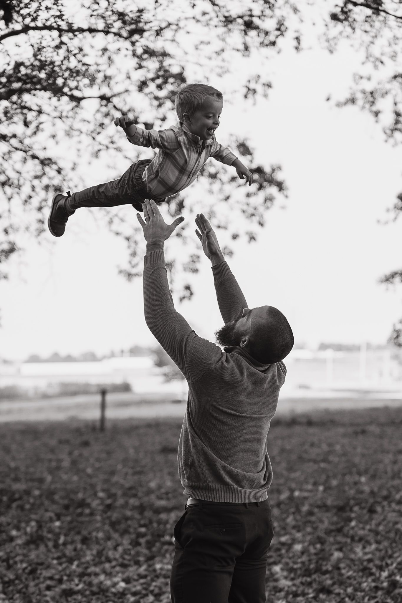 Black and white sequence shows a person lifting and playing with a baby against a rural outdoor backdrop.