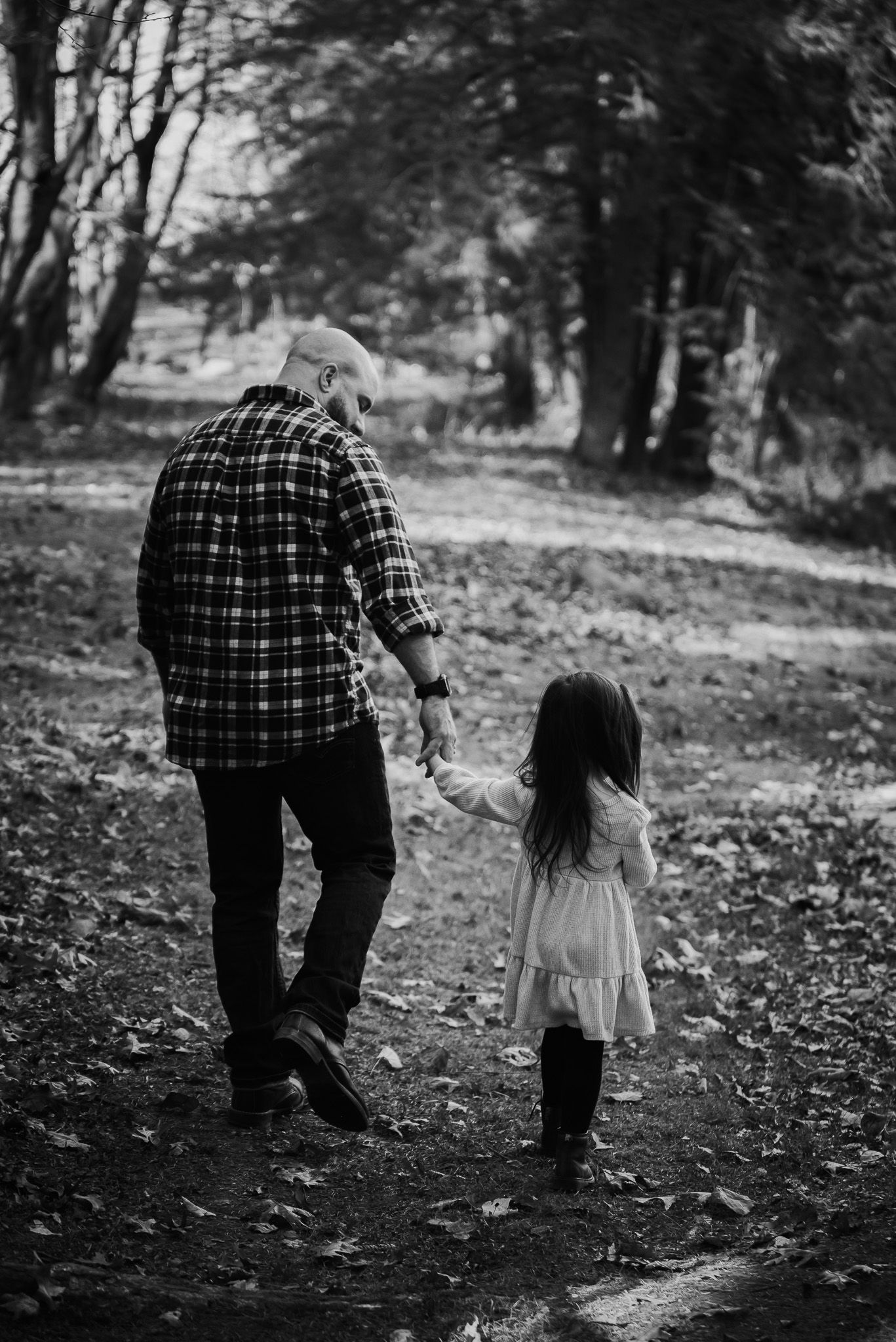Black and white image of parent and child walking hand in hand through forest path.