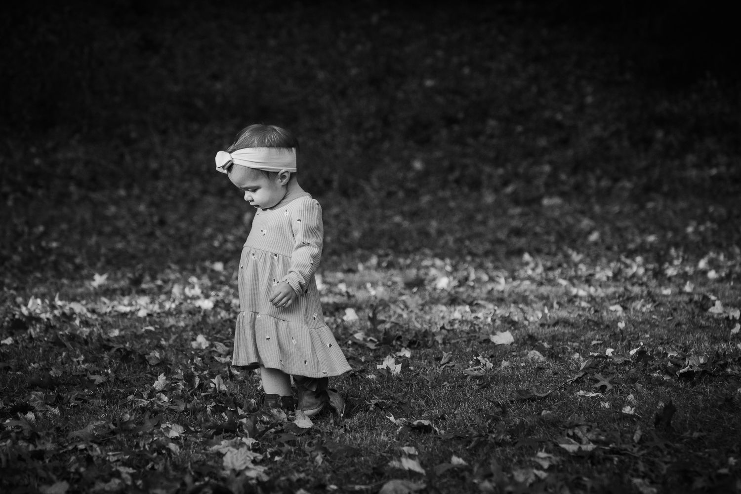 Black and white photo of child playing in fallen autumn leaves.