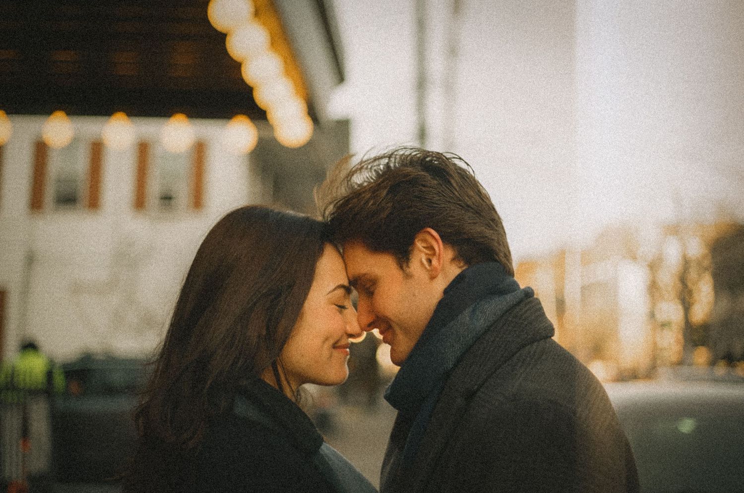 Romantic couple in winter coats share an intimate moment at sunset with soft lighting and warm tones.