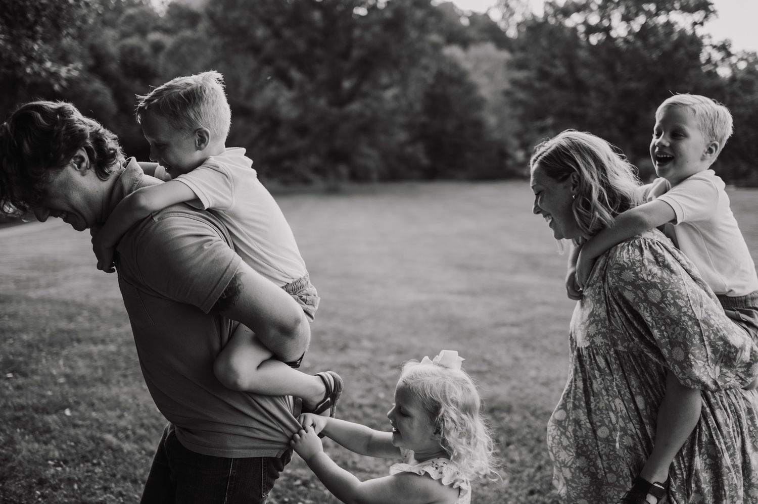 Black and white family photo of parents carrying children outdoors in a park setting.