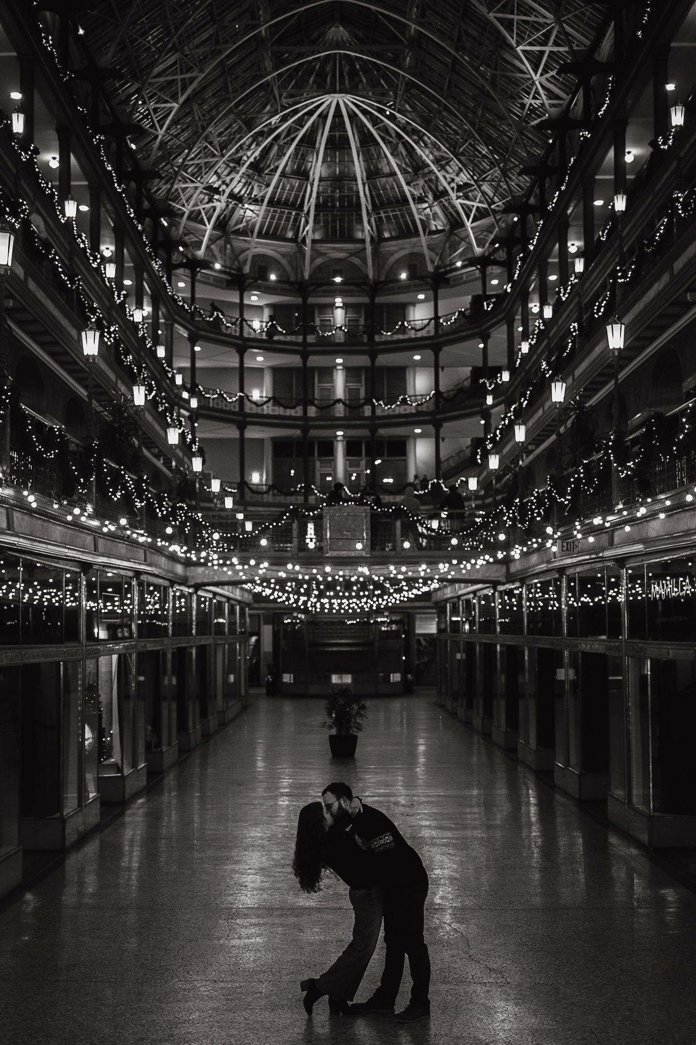 Black and white panoramic view of an ornate indoor arcade with twinkling string lights creating a magical ceiling display.