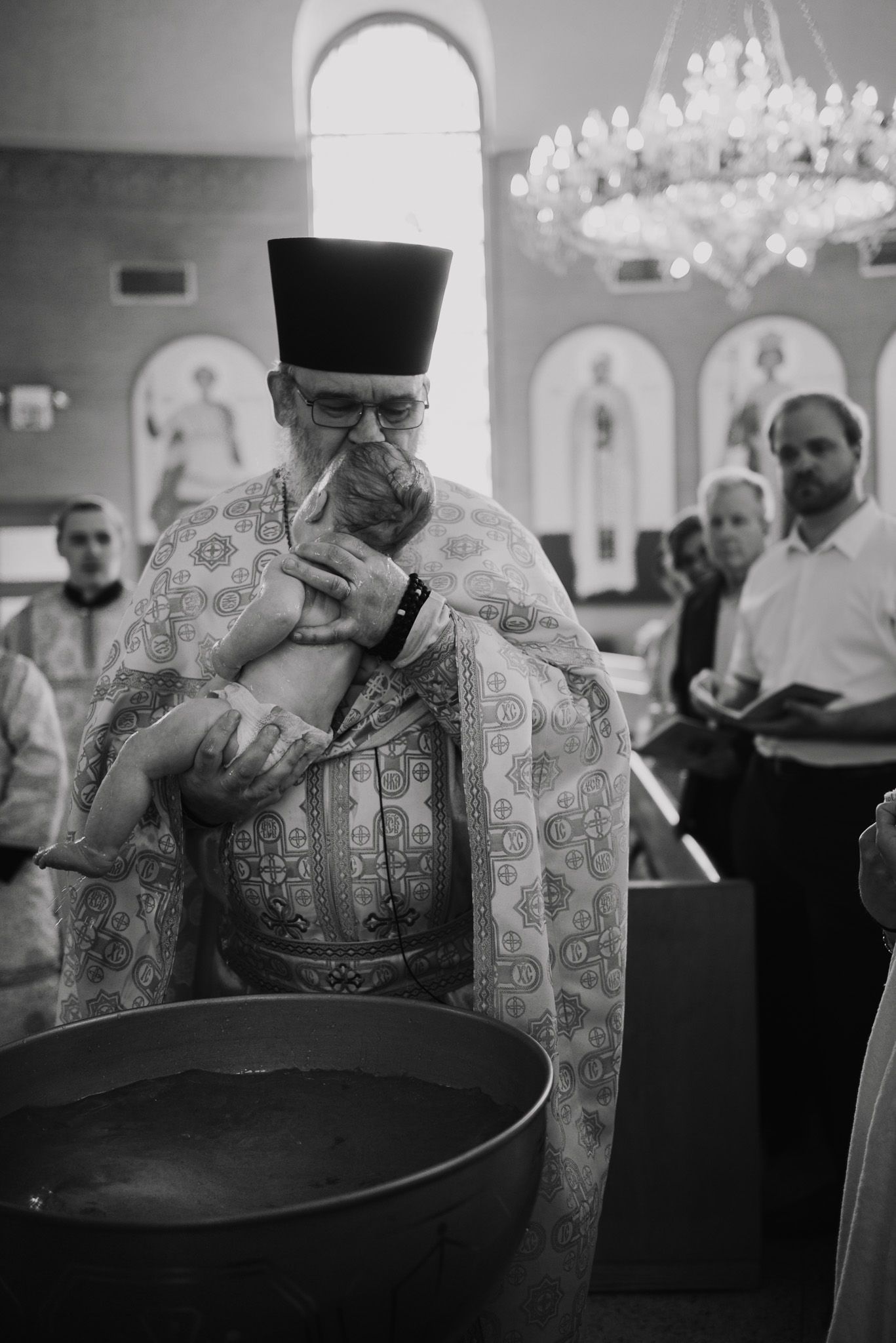 Orthodox priest in traditional robes performs religious ceremony in church setting.