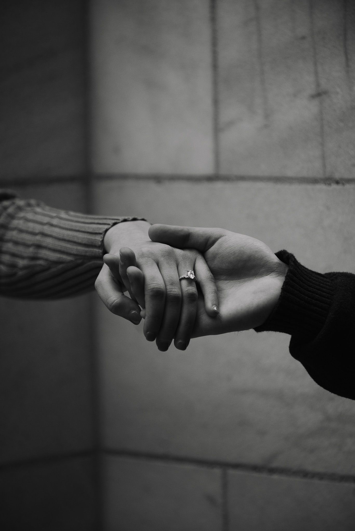 Two hands gently clasping together with an engagement ring visible in black and white.