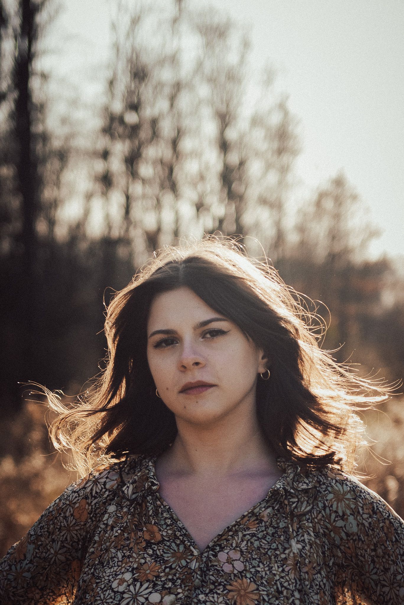 Backlit outdoor portrait with flowing hair and patterned dress at golden hour.