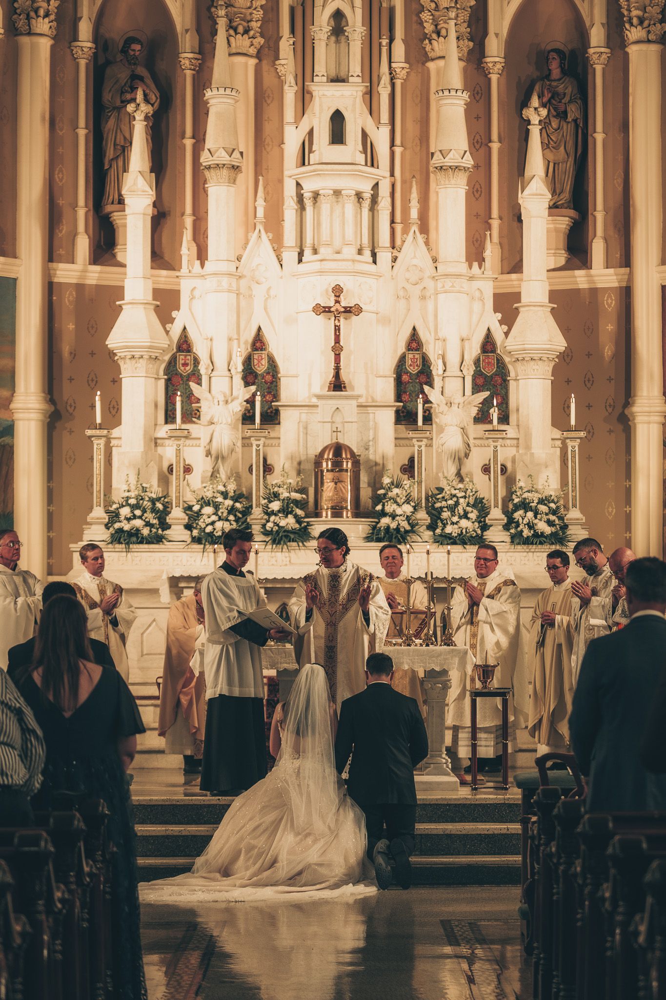 Traditional Catholic church wedding ceremony with golden altar and floral decorations.