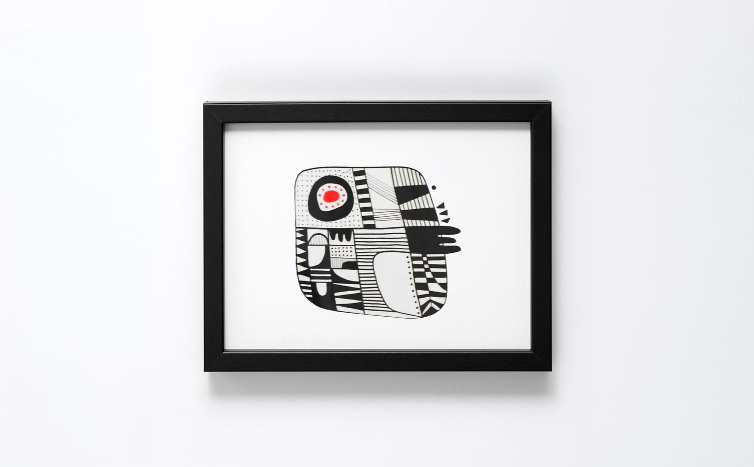 Abstract geometric art print in black, white, and red, displayed in a black frame on a white wall.