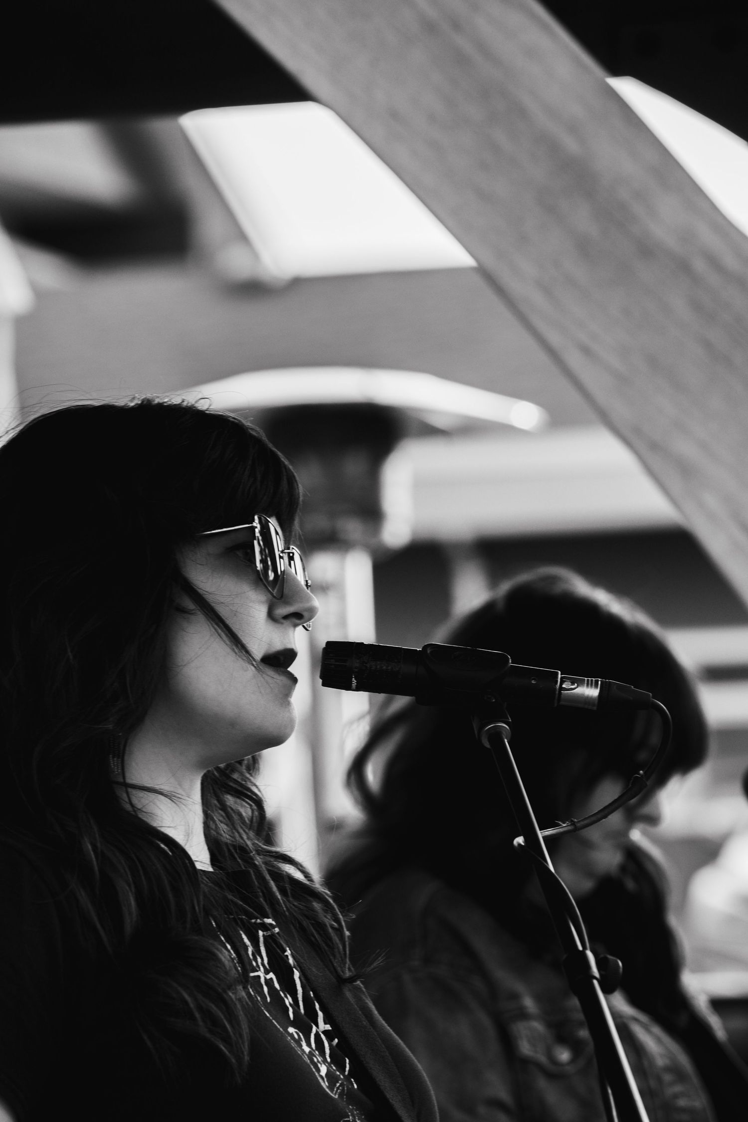 Black and white profile of woman with sunglasses singing into a microphone on stage.