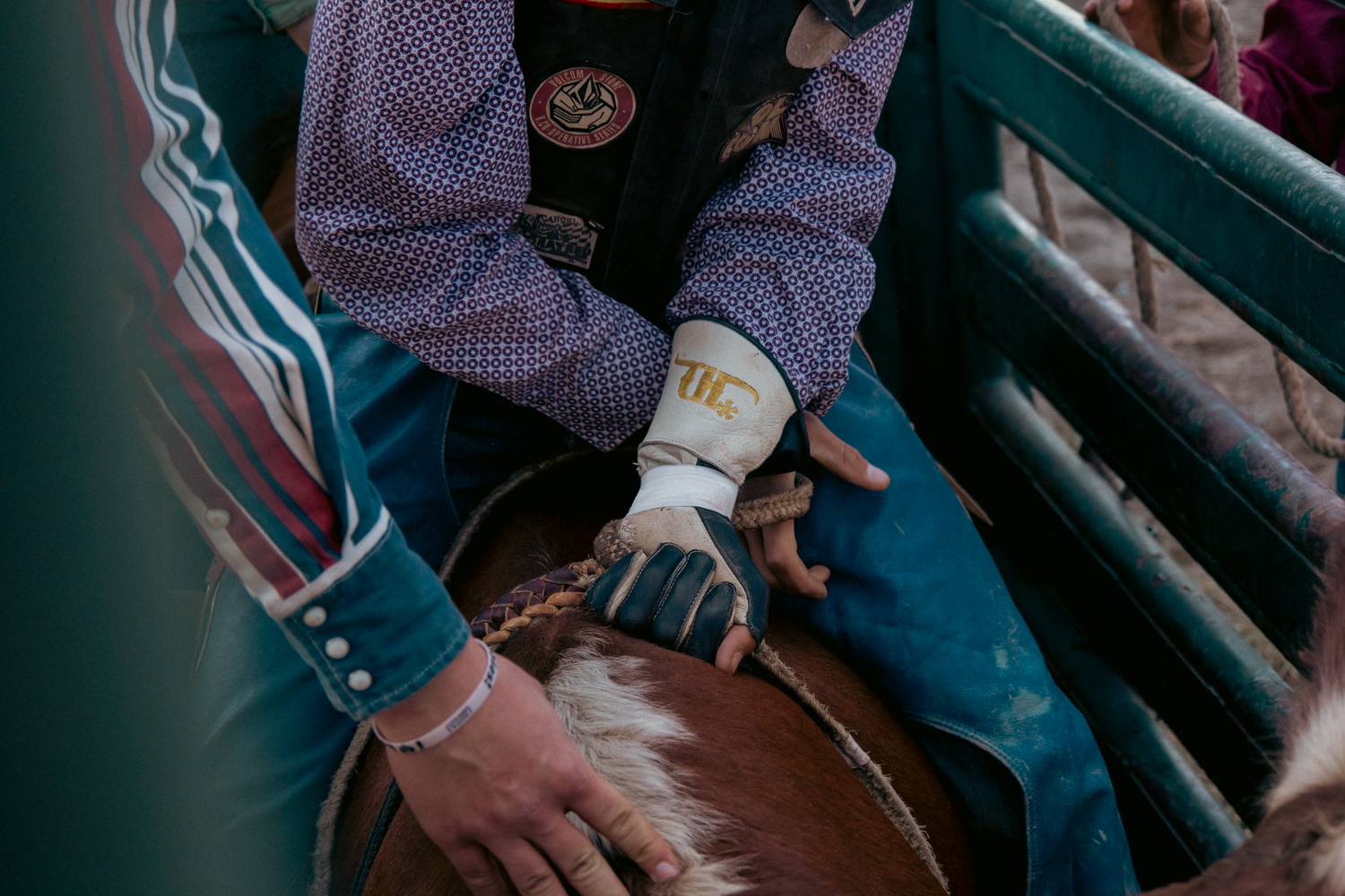 A rodeo cowboy grips a bull rope with gloved hands, preparing for a bull riding event at a rodeo.