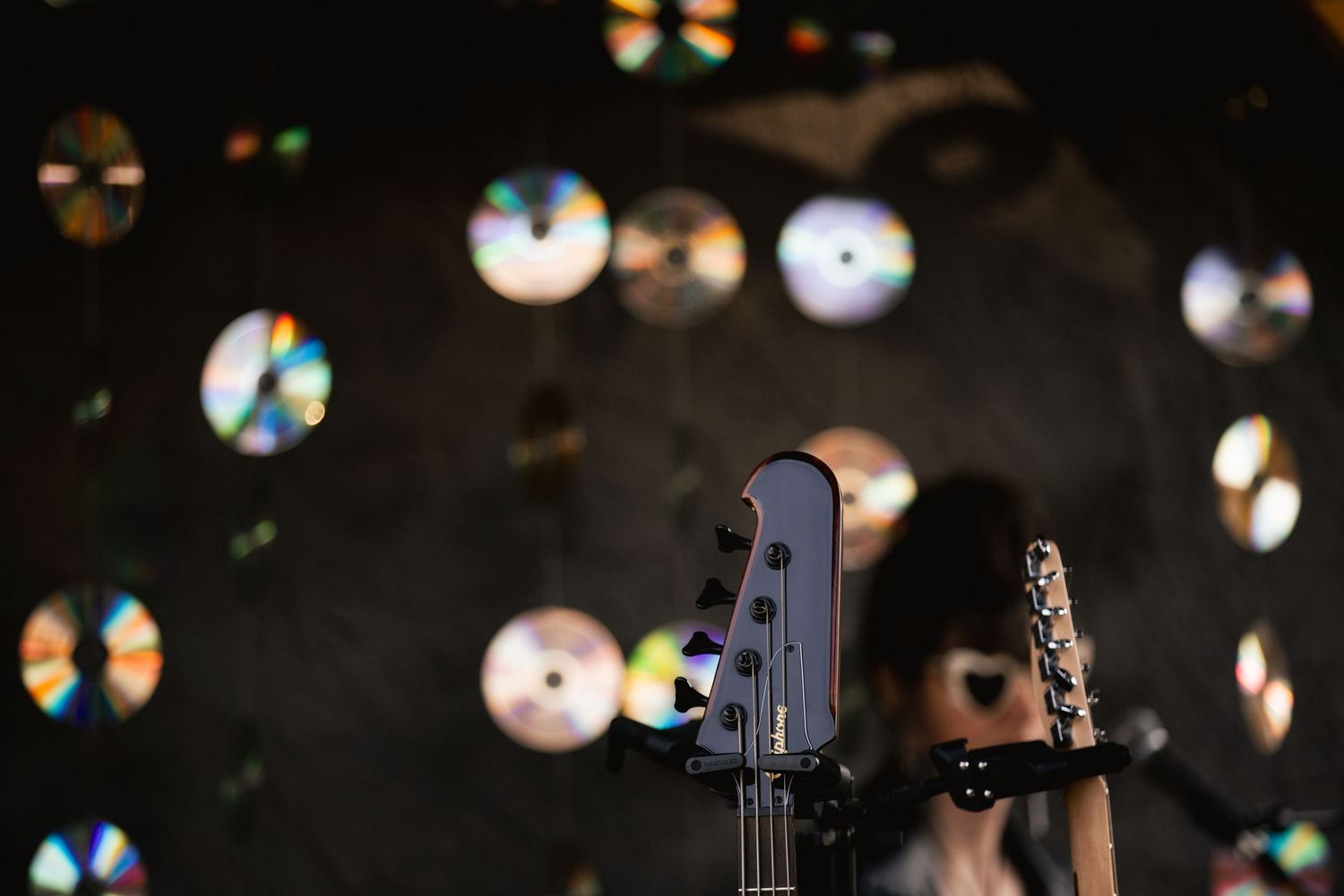 Electric guitar in foreground with colorful CDs hanging as backdrop in a dark venue.