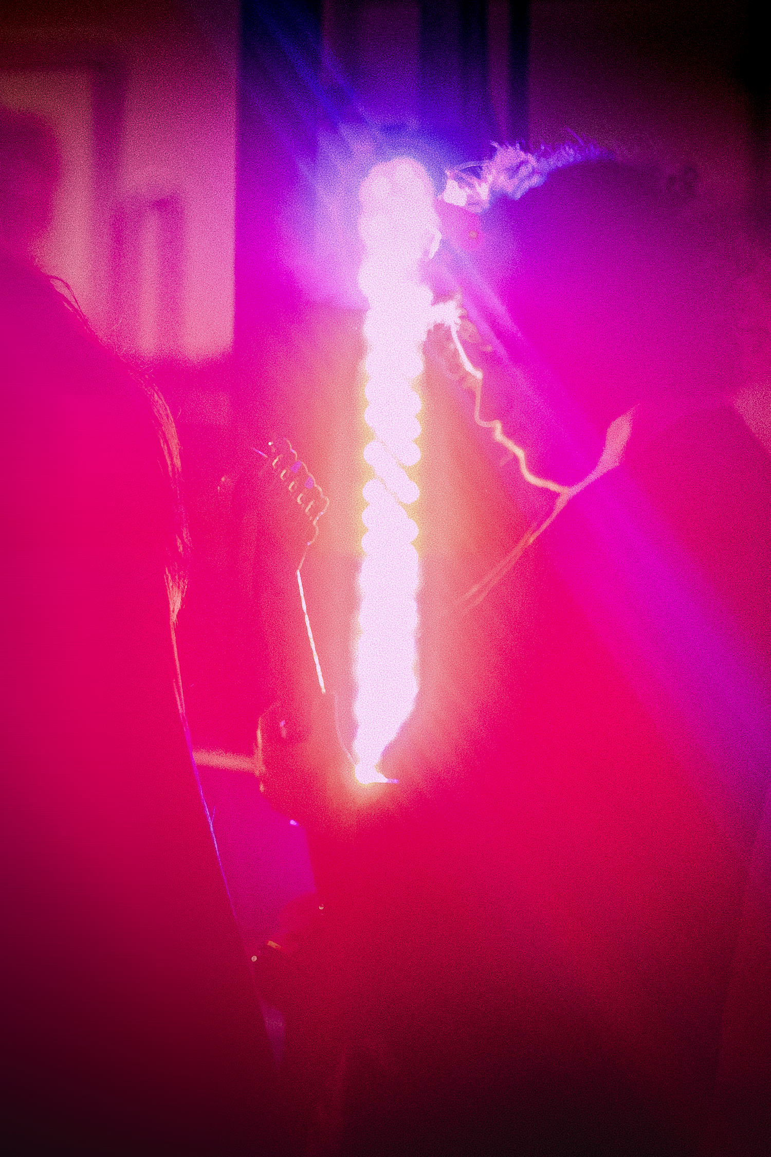 Guitarist performing on stage surrounded by intense pink and white light beams during live rock concert.