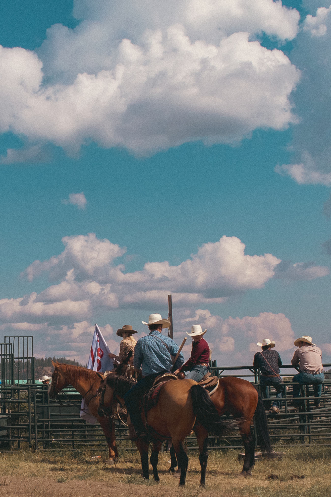 Cowboys on horseback holding a flag at a rodeo arena under dramatic blue sky with white clouds.